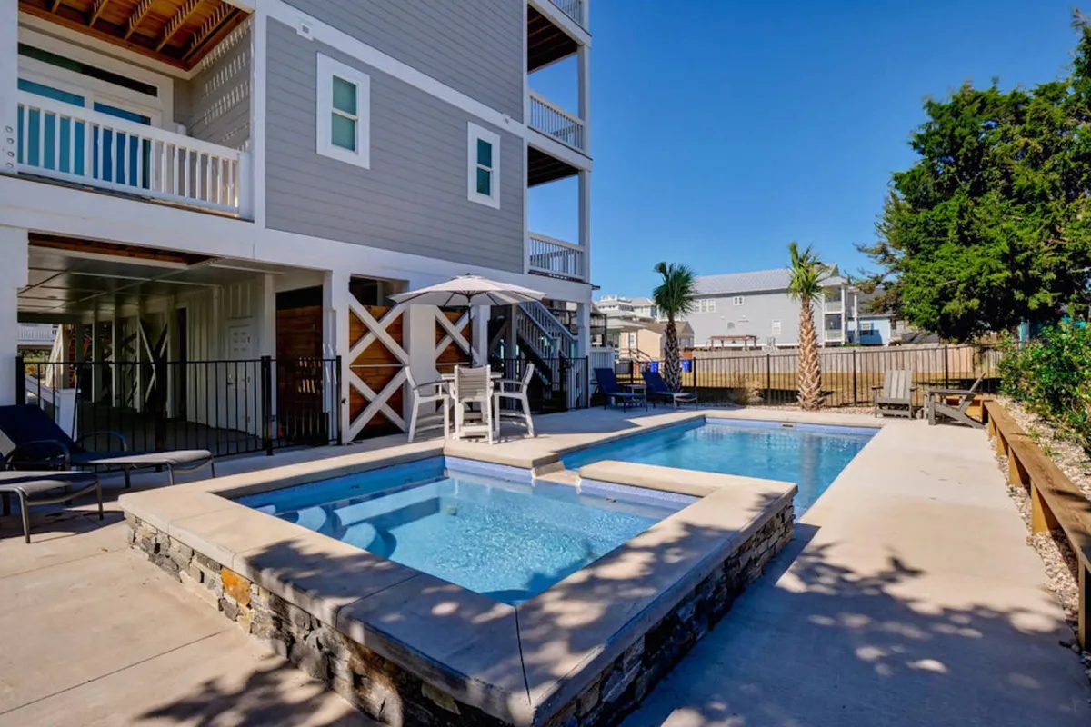 This exterior shot showcases the resort-like swimming pool surrounded by inviting lounge chairs, lush landscaping, and shaded seating areas. The space is designed for relaxation, sunbathing, and socializing, embodying the leisurely, high-end amenities highlighted in the section.