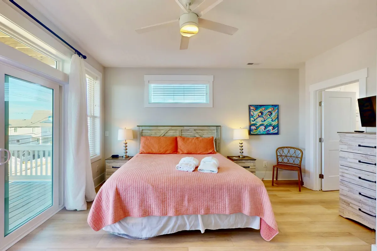 A serene bedroom with coral bedding, tasteful artwork, and a large window that allows sunlight to fill the space. The setting is tranquil, perfect for reading or enjoying a morning coffee.