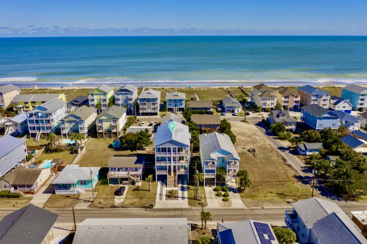 A wide exterior view featuring beachfront properties with clear ocean vistas and a row of homes, evoking a sense of the vibrant beach neighborhood. The image conveys the atmosphere of being moments from the sand and surf, ideal for sunrise walks or sandcastle-building family adventures.