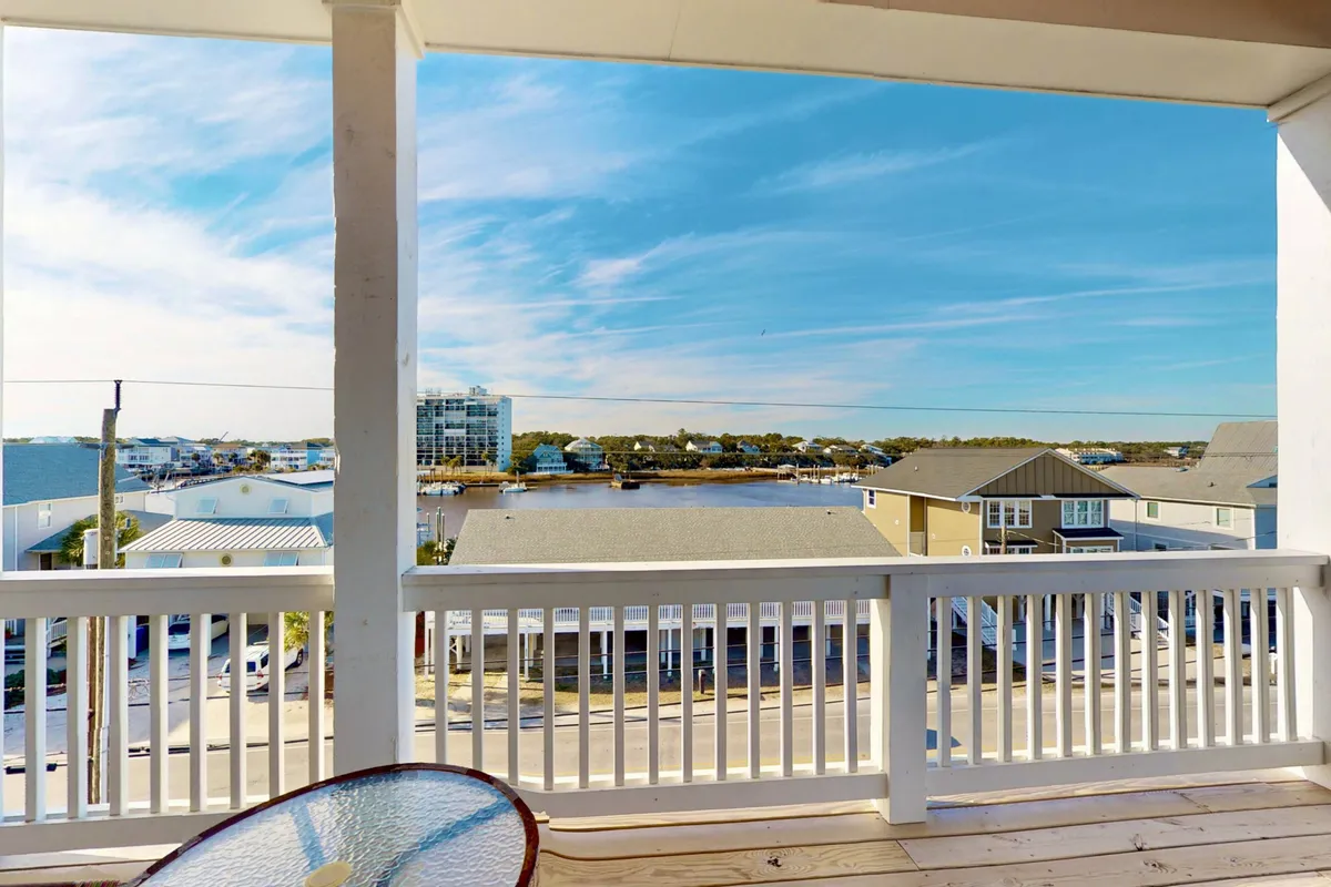 A peaceful waterfront view featuring the blue sky and tranquil water, with a balcony railing in the foreground. The vantage point invites relaxation and contemplation, suggesting a close connection to outdoor aquatic experiences.