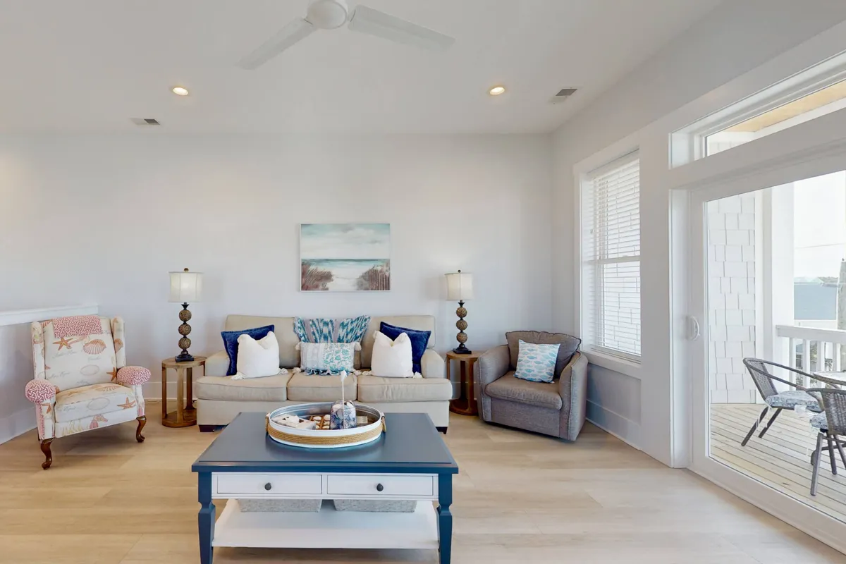 This image features a cozy living room with a comfortable sofa adorned with decorative pillows, armchairs, a coffee table with a tray, and tasteful artwork. Large windows open to the outdoors, letting in plenty of light and offering views, while the space is inviting for family relaxation, movie nights, or friendly gatherings.