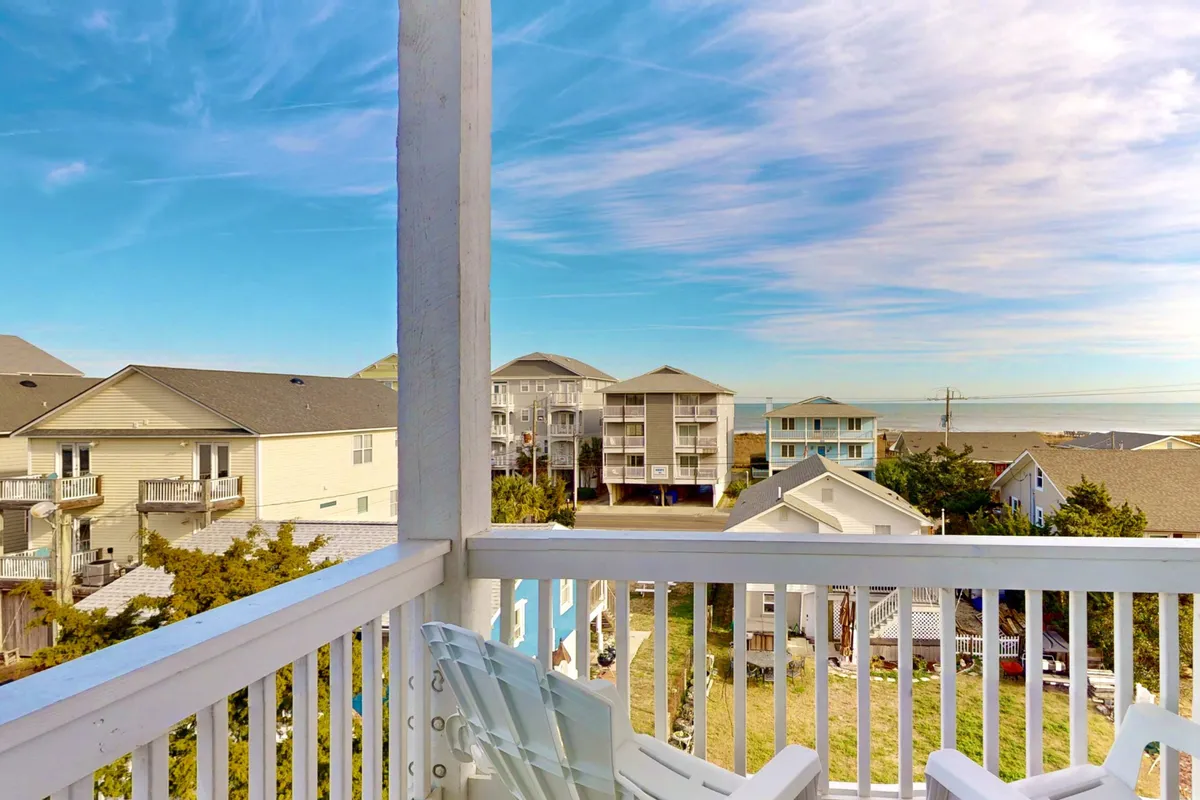 A tranquil view from a private balcony, featuring a sturdy railing, sweeping sea views, and glimpses of neighboring houses. The angle captures the serene water and sky, evoking the feeling of enjoying a morning coffee or watching the sunset over the ocean.