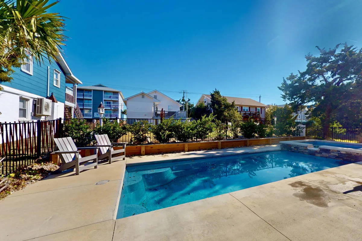 The image displays an inviting exterior scene featuring a swimming pool surrounded by lounge chairs and a landscaped garden. The tranquil setting suggests ample opportunities for swimming, sunbathing, and outdoor dining, perfect for family gatherings or relaxing in a resort-like atmosphere.